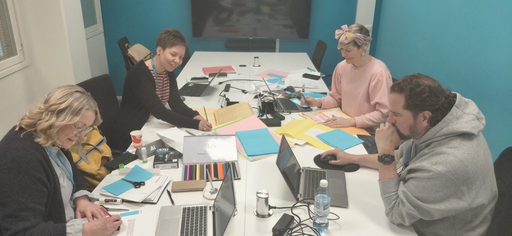 Neljä henkilöä askartele pöydän ääressä kartongista lappuja.