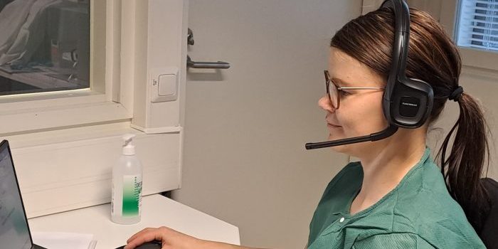 Sairaanhoitaja tietokoneen äärellä headset päässä.