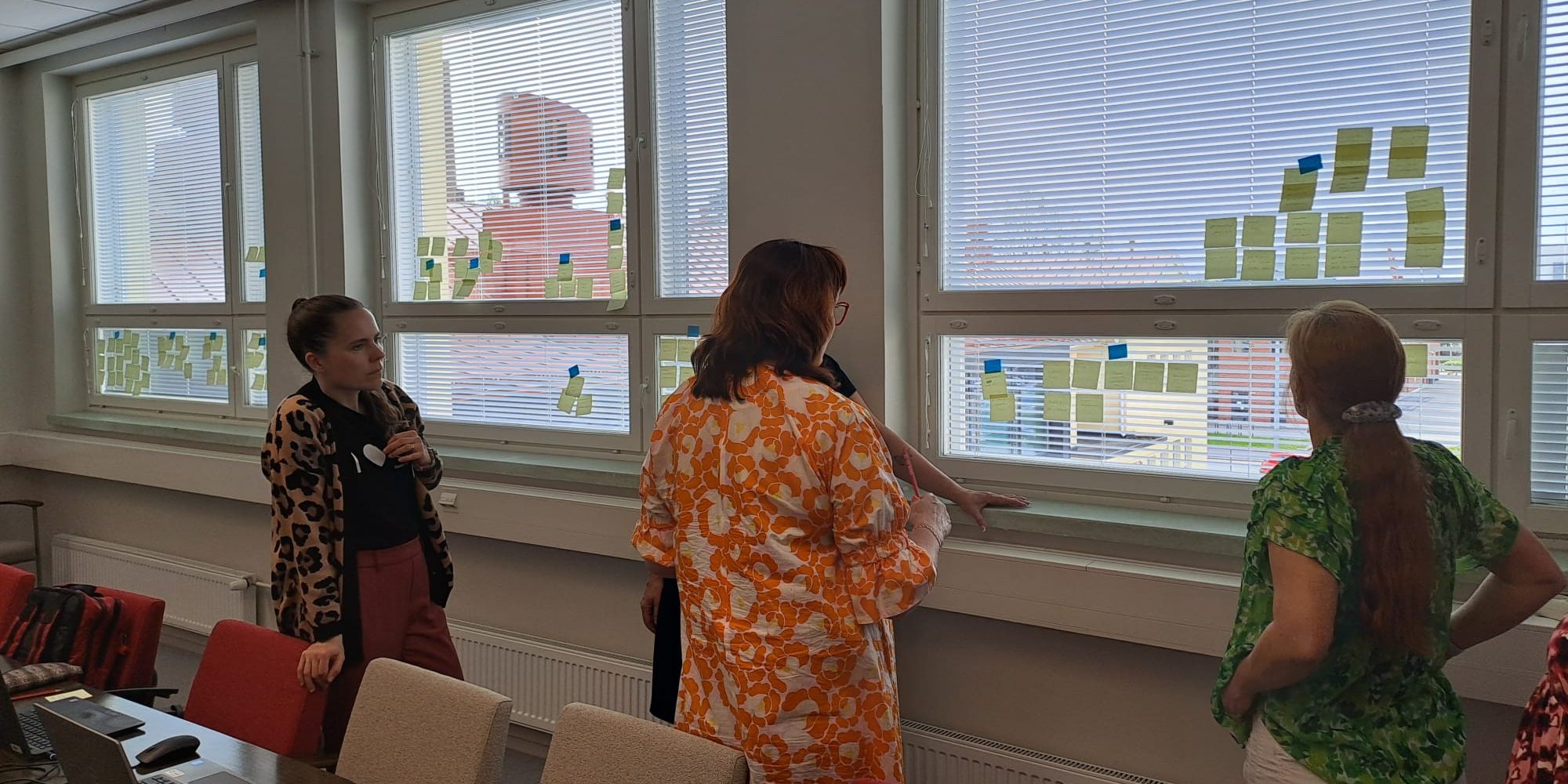 Kolme ihmistä tarkastelee ikkunaan kiinnitettyjä post it lappuja.